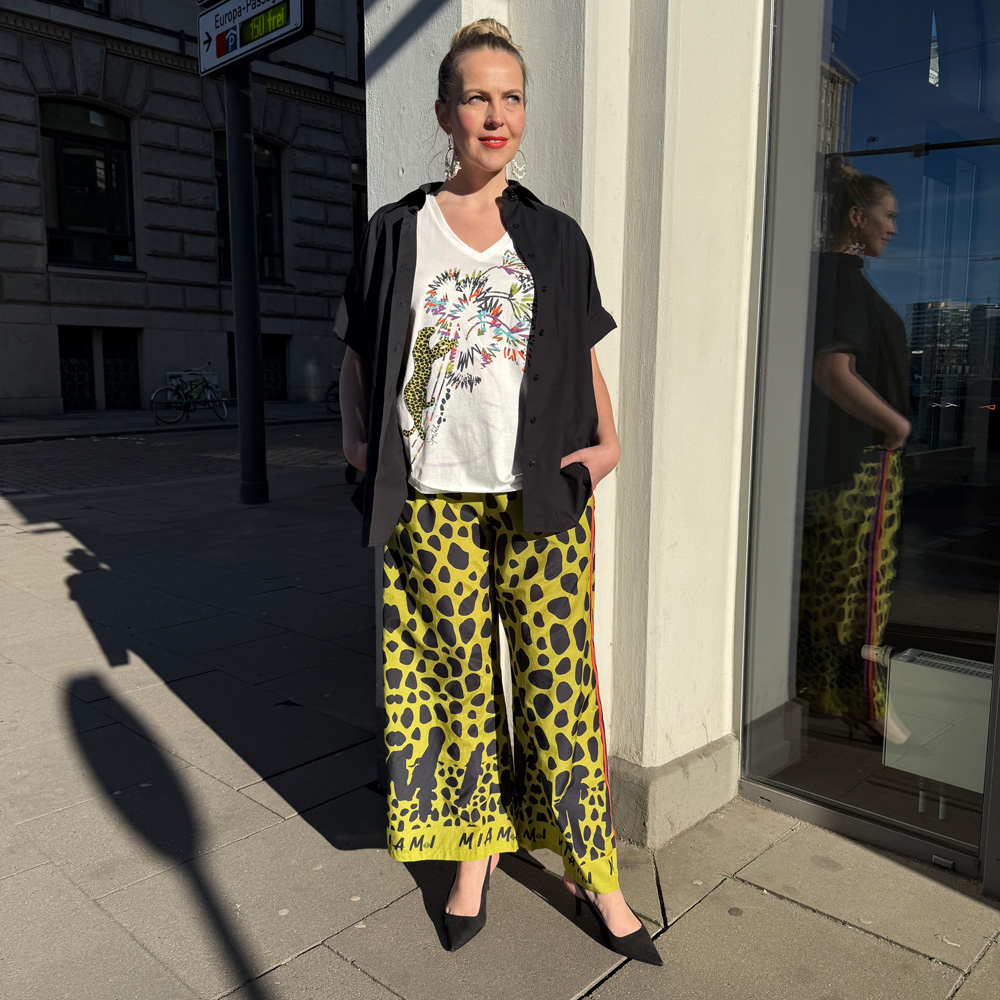 Frau in modischem Outfit vor einem Geschäft in der Innenstadt, präsentiert moderne mode für große größen freiburg in einem lässigen, farbenfrohen Look.