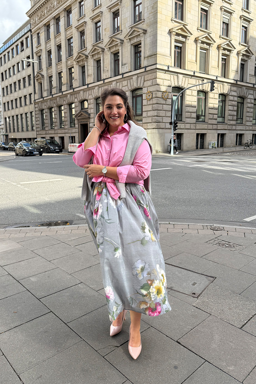 Stilvolle Mode in großen Größen in Oldenburg, eine Frau in floralem Rock und pinker Bluse posiert in der Innenstadt.