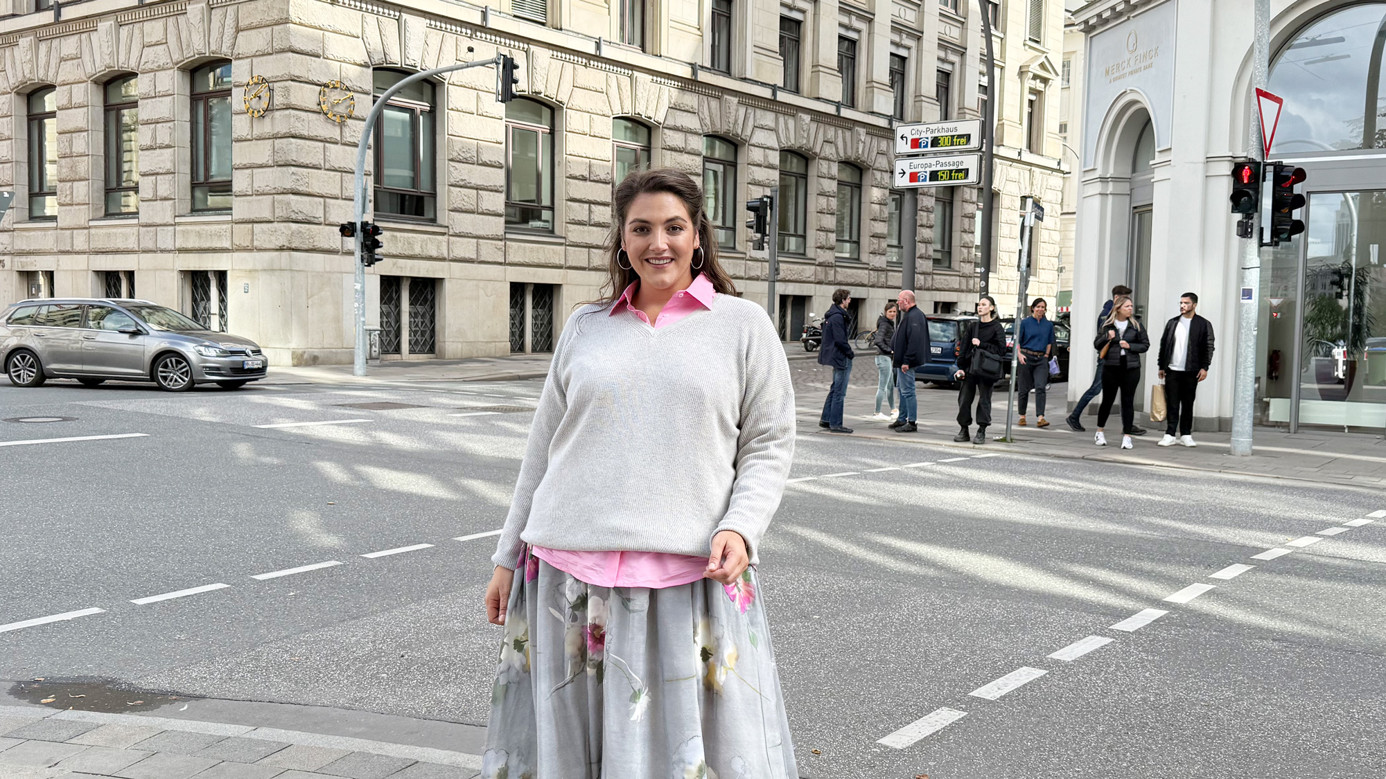Frau trägt hellen Pullover, rosa Bluse und weiten Rock in der Innenstadt, elegante Damenmode Übergrößen Nürnberg mit femininem, modernem Stil.