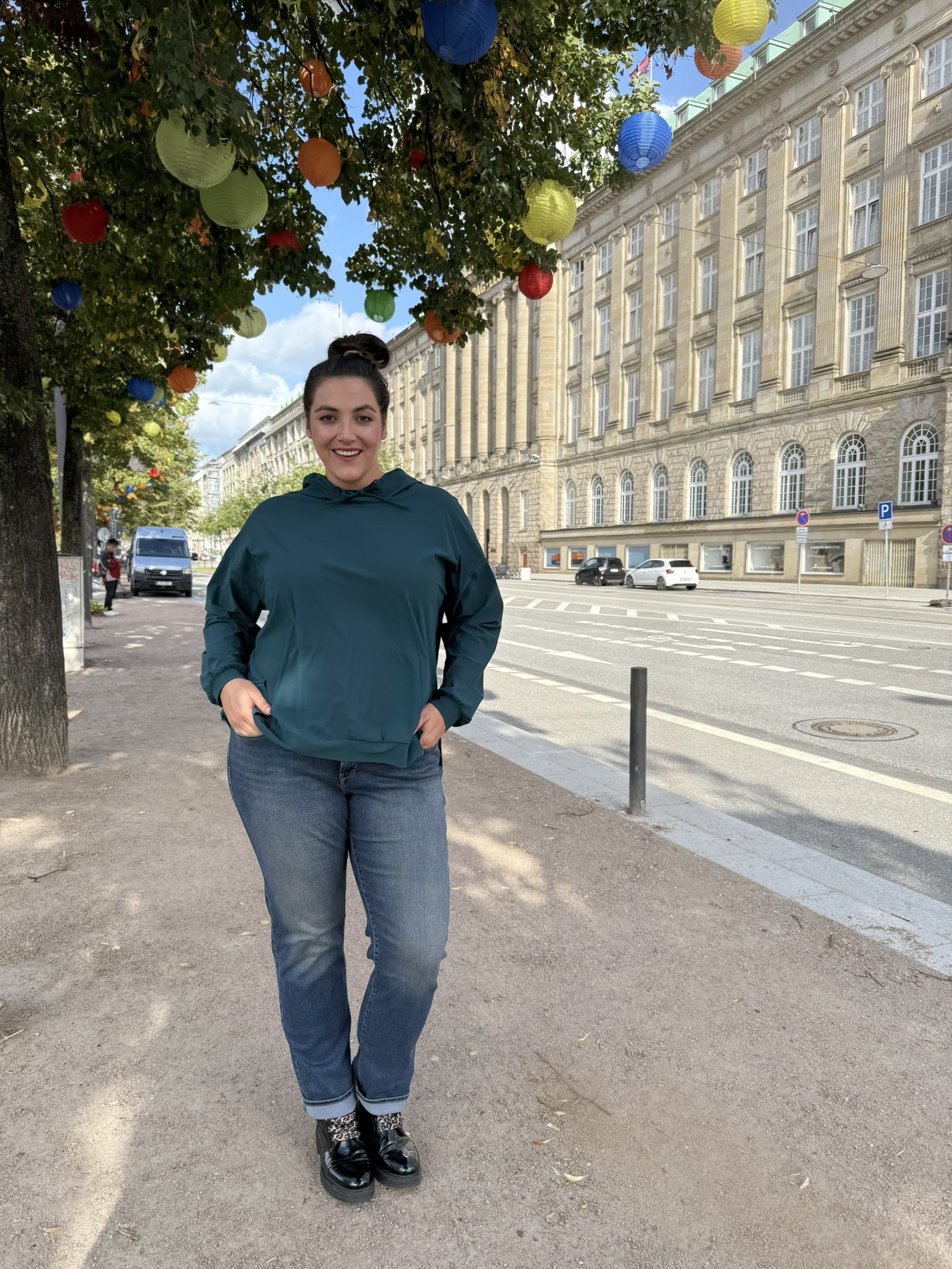 Mode für mollige in Dresden mit lässigem Outfit unter bunt geschmückten Bäumen.
