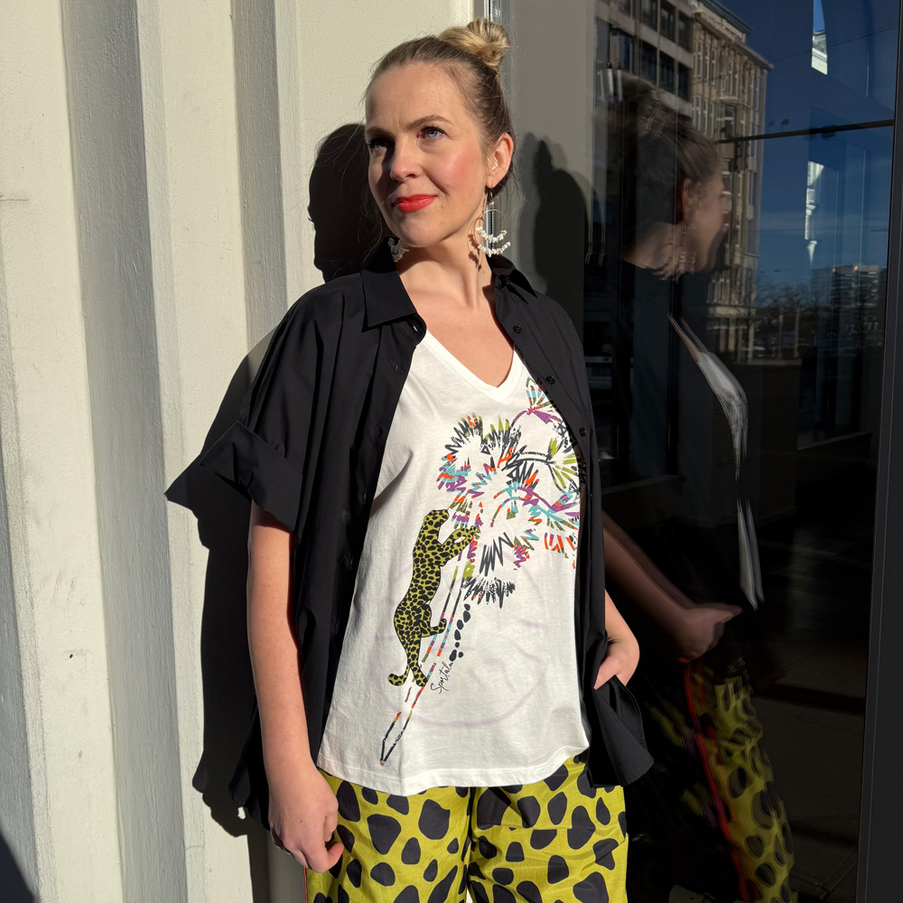 Moderne große größen damen in bremen, gezeigt mit einer stylischen Kombi aus gemustertem Shirt, schwarzer Bluse und Statement Hose in der Sonne.