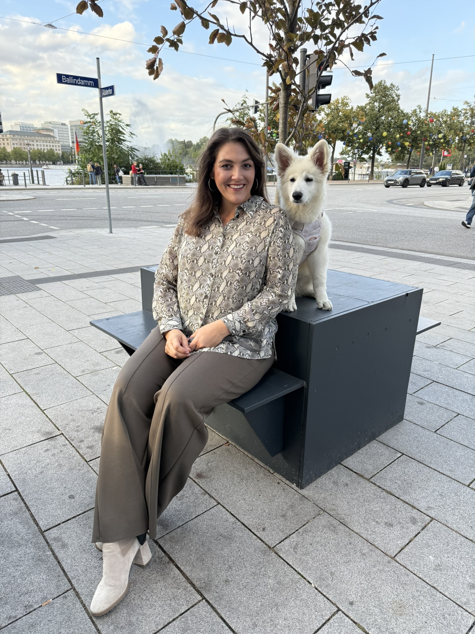 Frau sitzt mit einem weißen Hund am Ballindamm, stilvolle Plus Size Münster Mode in entspannter, eleganter Kombination.