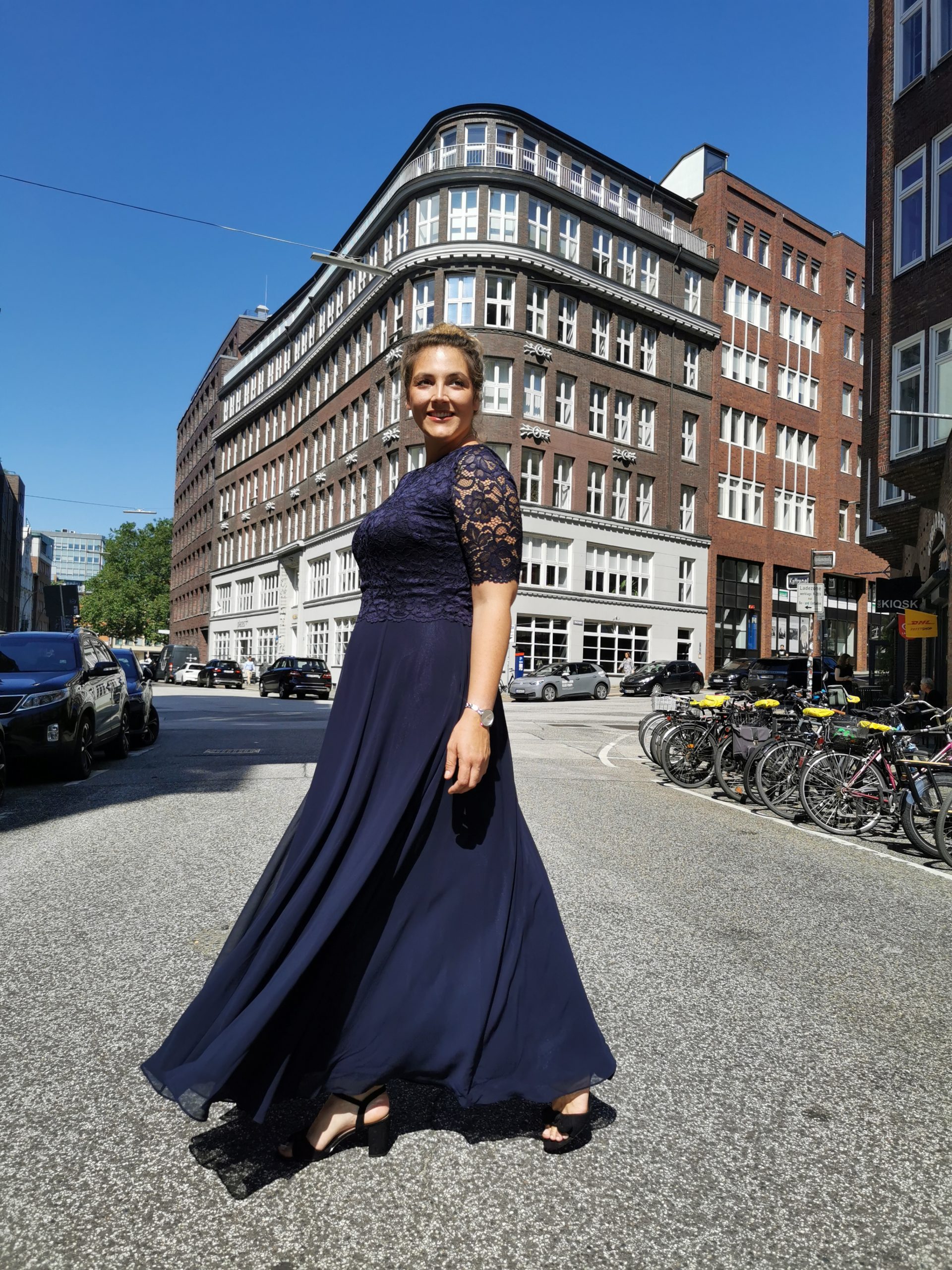 Elegante Abendmode große Größen Hamburg mit langem Spitzenkleid in Blau auf der Straße.