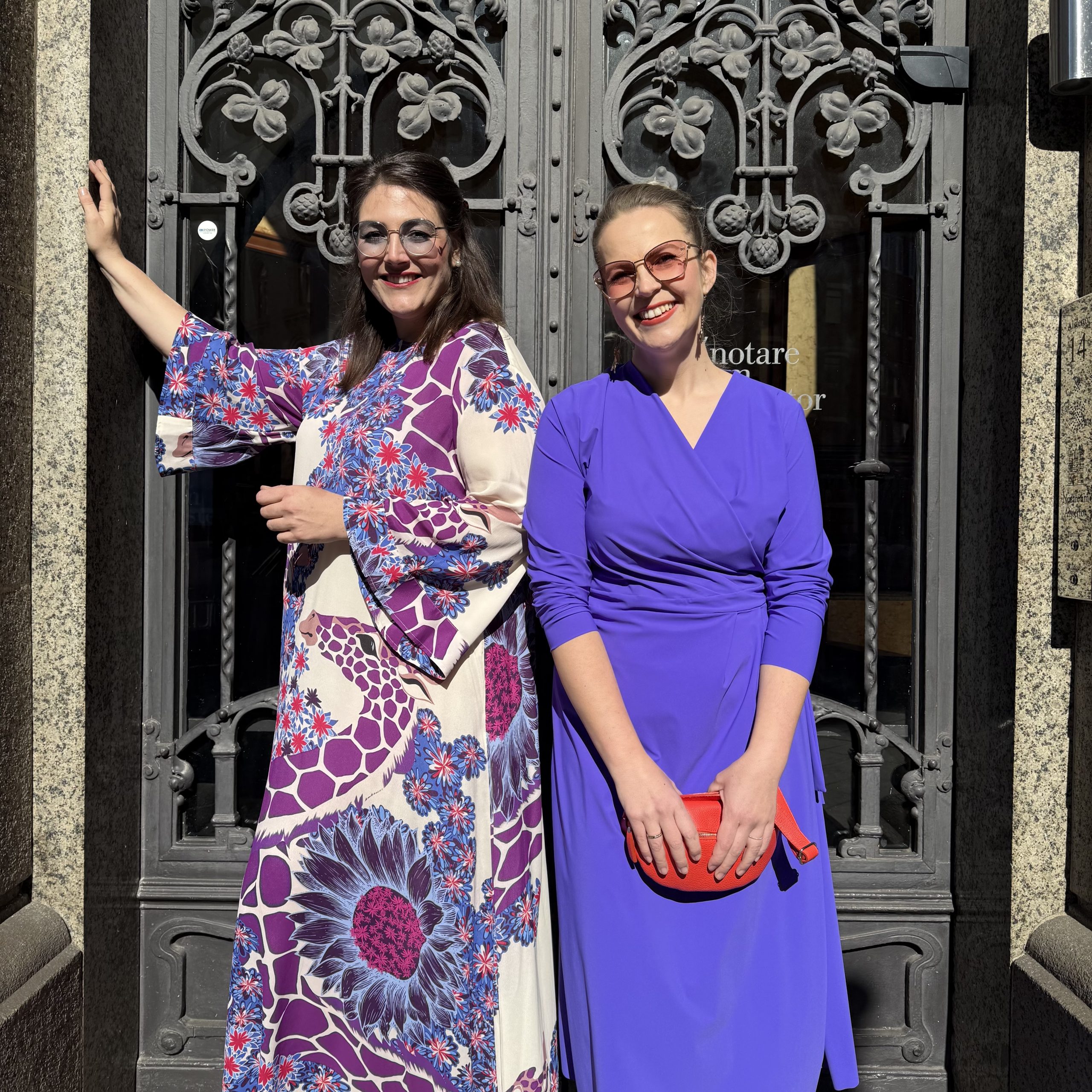 Abendmoden große Größen Hamburg mit farbenfrohen Kleidern vor historischer Tür.