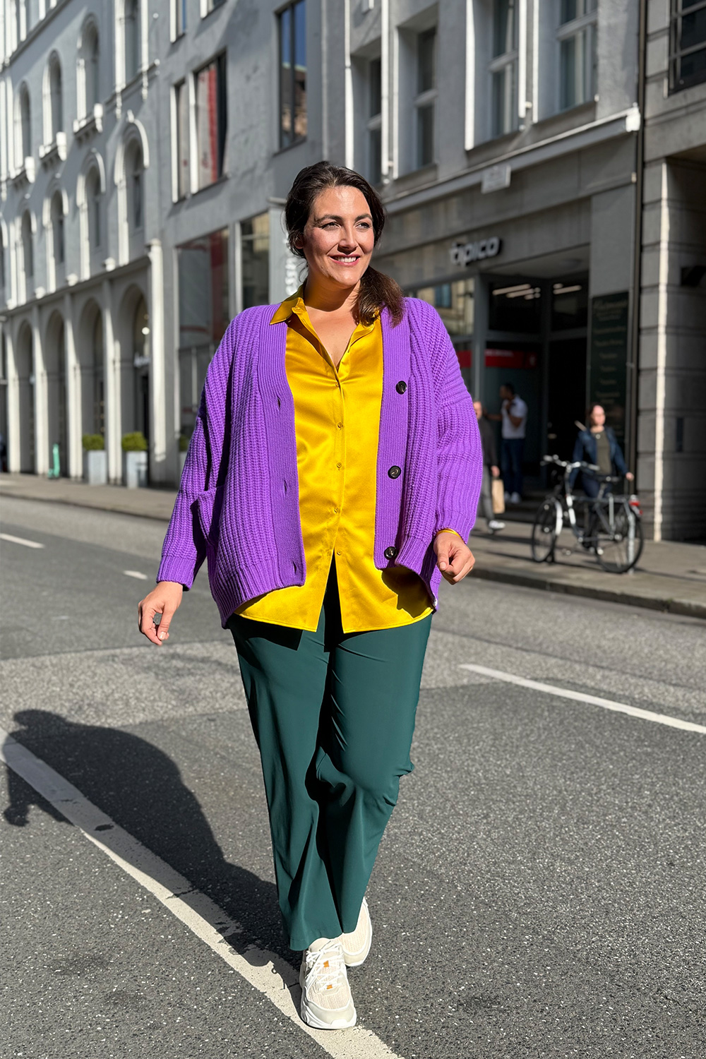 Damenmode große Größen Lübeck, Kundin in gelber Seidenbluse, lila Grobstrickcardigan und dunkelgrüner Marlenehose.