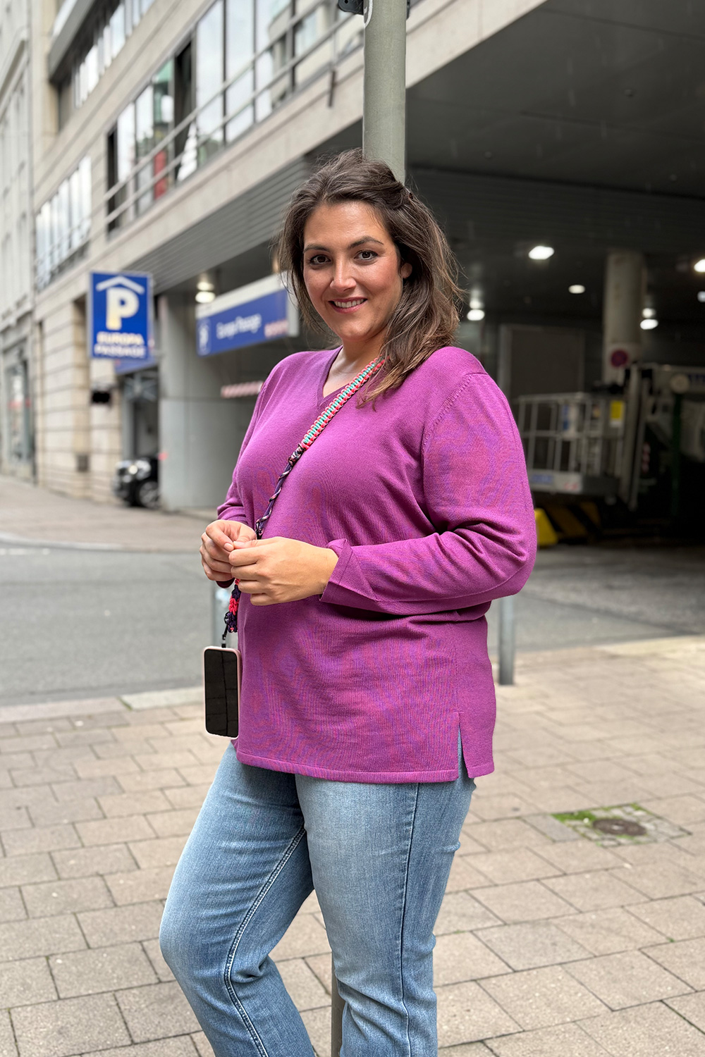 Kiel große Größen, Kundin in beerenfarbenem Feinstrickpullover mit V Ausschnitt und heller Bootcut Jeans