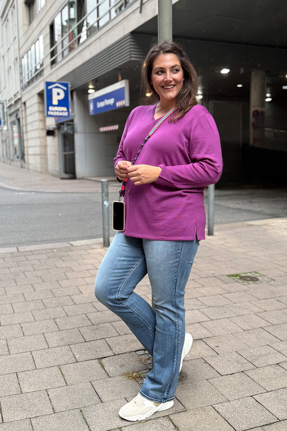 Mode für große Größen Lübeck am Beispiel eines Casual Looks mit magentafarbenem Pulli und blauer Schlagjeans.