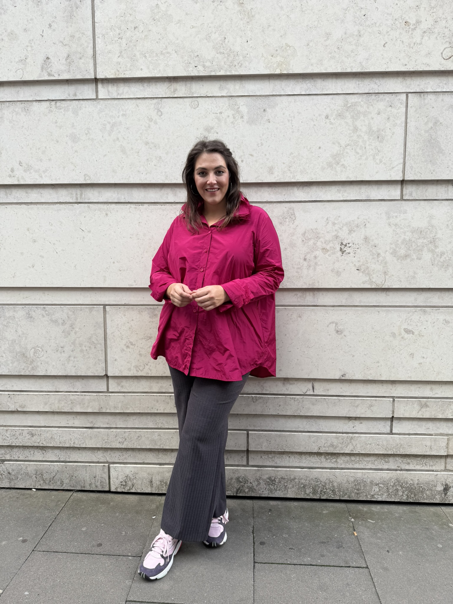 Übergrößen Braunschweig, Kundin in pinker Oversize Bluse, anthrazitfarbener Marlenehose und rosa Sneakern.