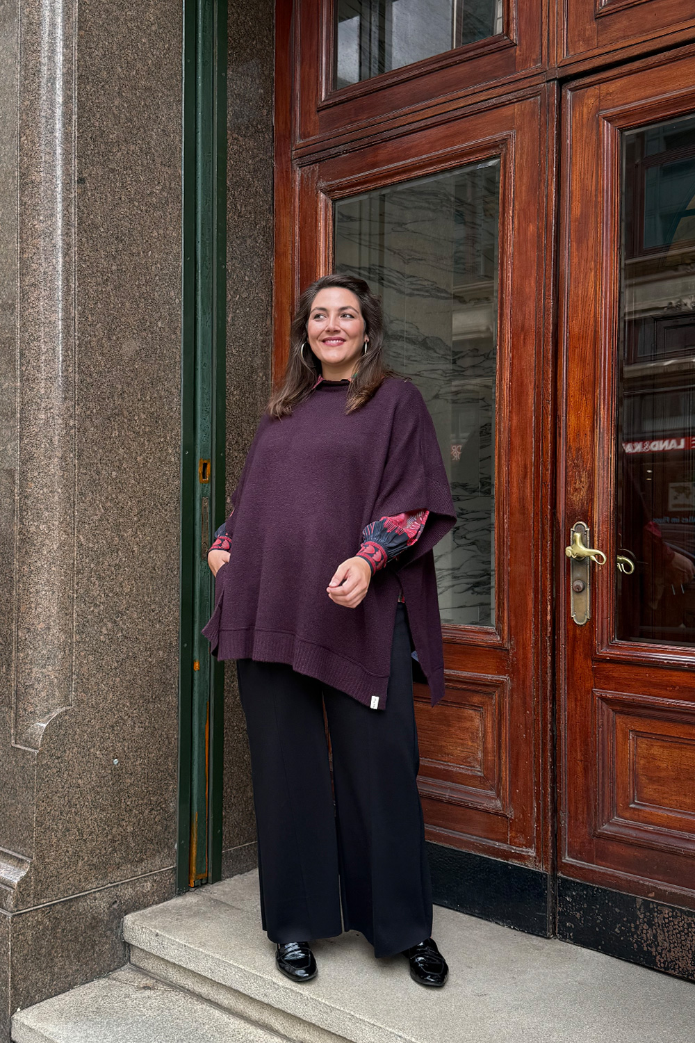 Übergrößen Lübeck am Beispiel eines Herbstlooks mit Wollponcho in Bordeaux, dunkler Stoffhose und Lackloafern.