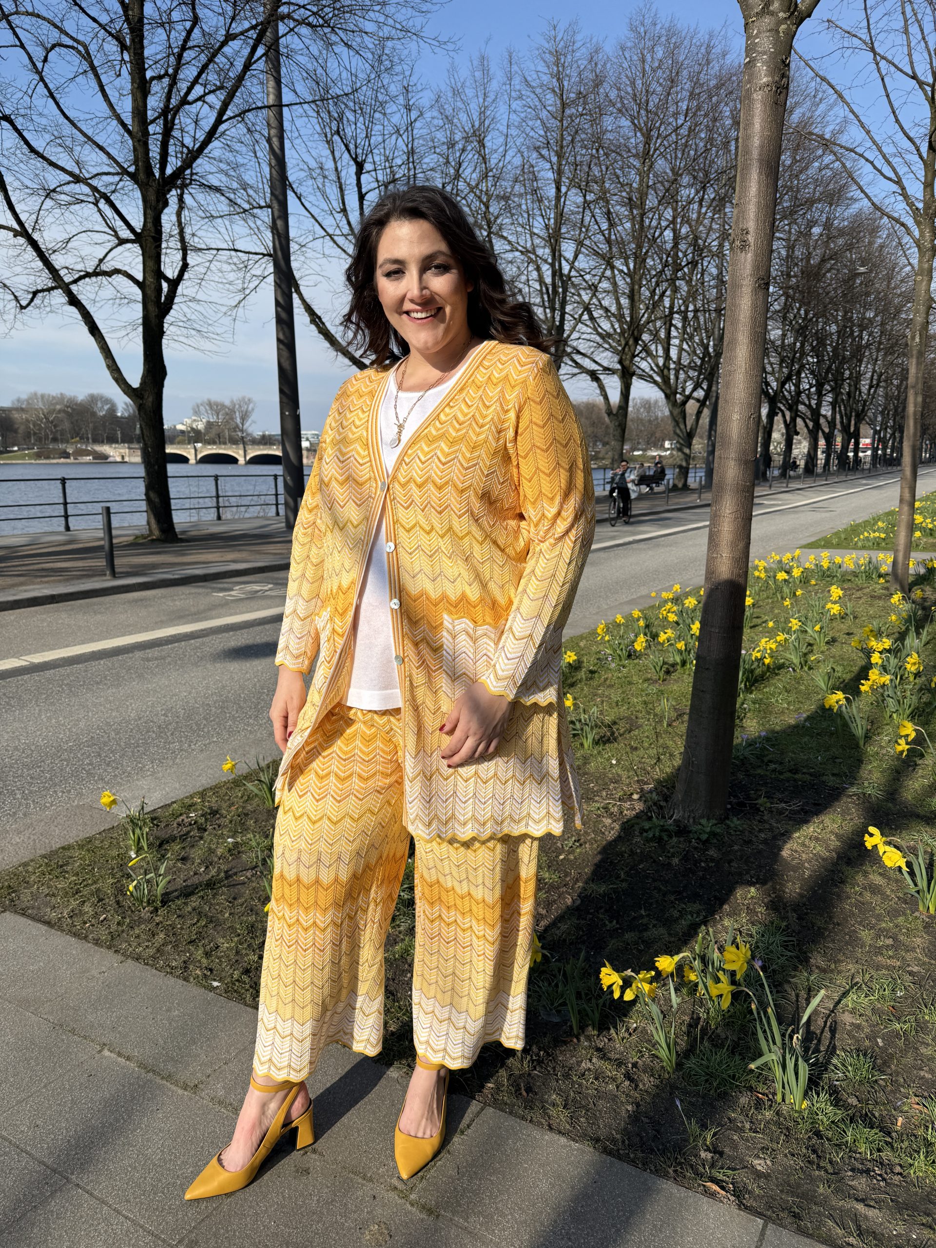 Große Größen in Essen: Frau trägt gelbes Strick-Zweiteiler-Set mit Cardigan und gelben Slingback-Pumps