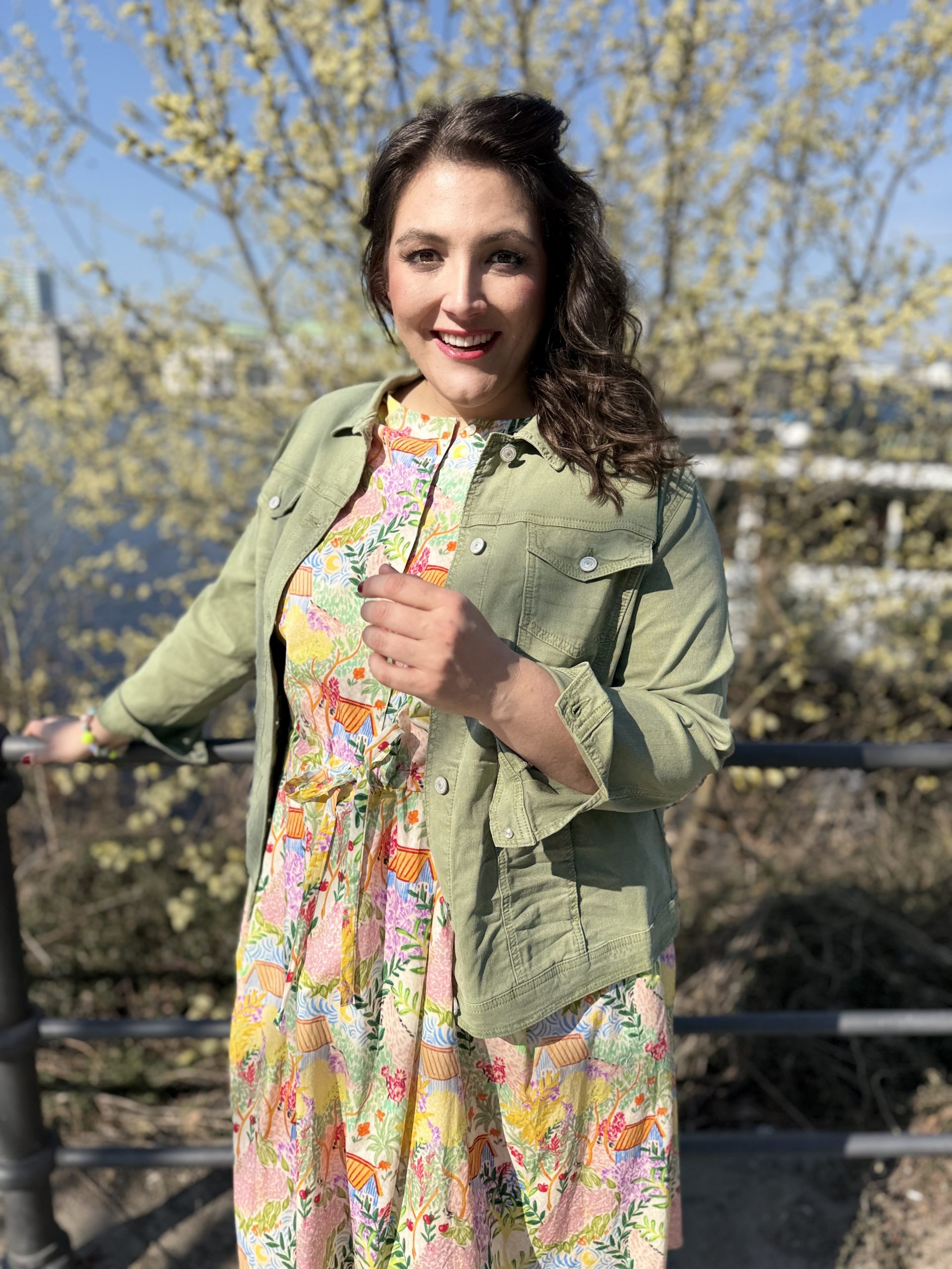 Große Größen in Frankfurt: Frau trägt buntes Blumenkleid mit olivgrüner Jeansjacke am Main im Frühling