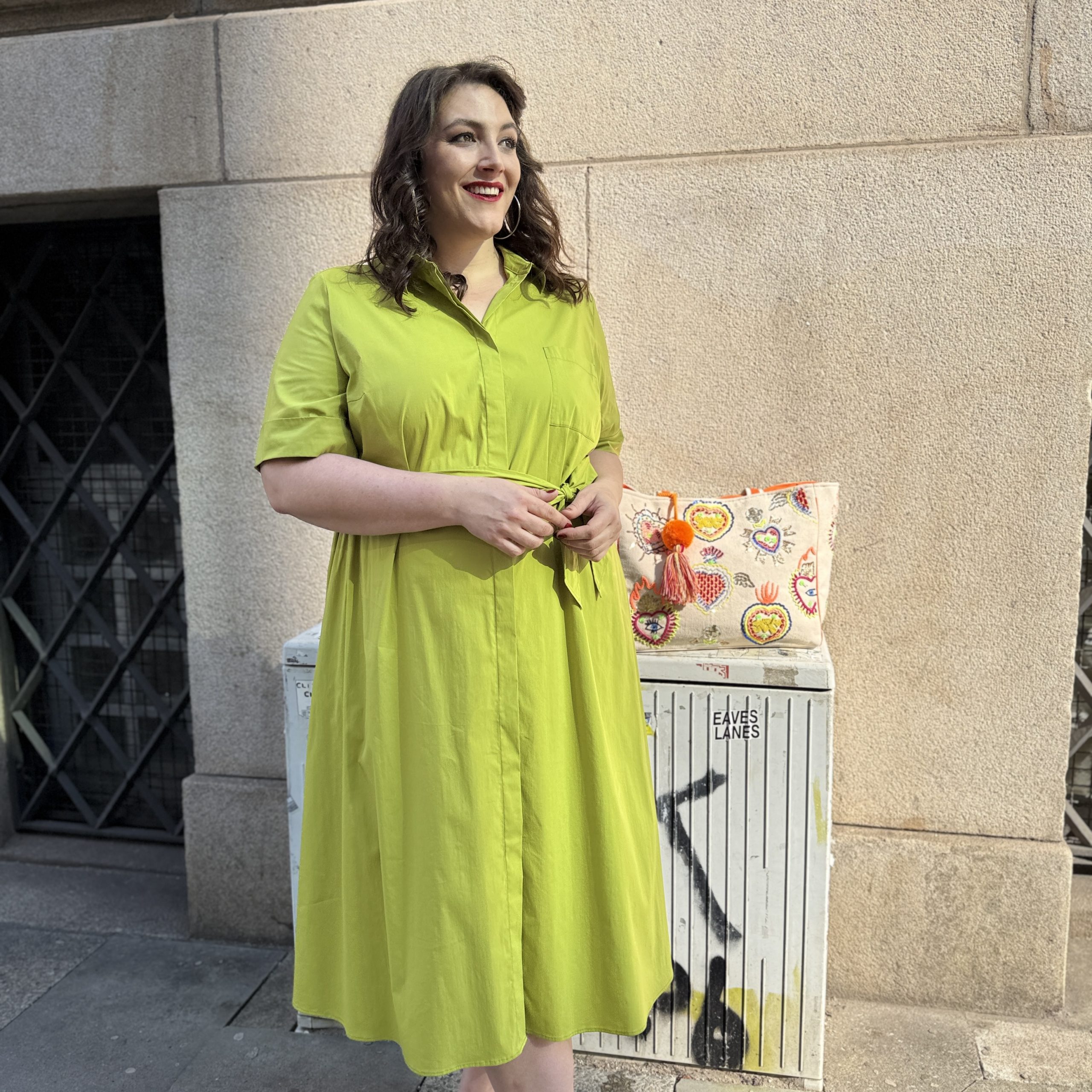 Große Größen in Lübeck: Frau trägt lindgrünes Hemdblusenkleid mit Bindegürtel und bunter Clutch im Streetstyle