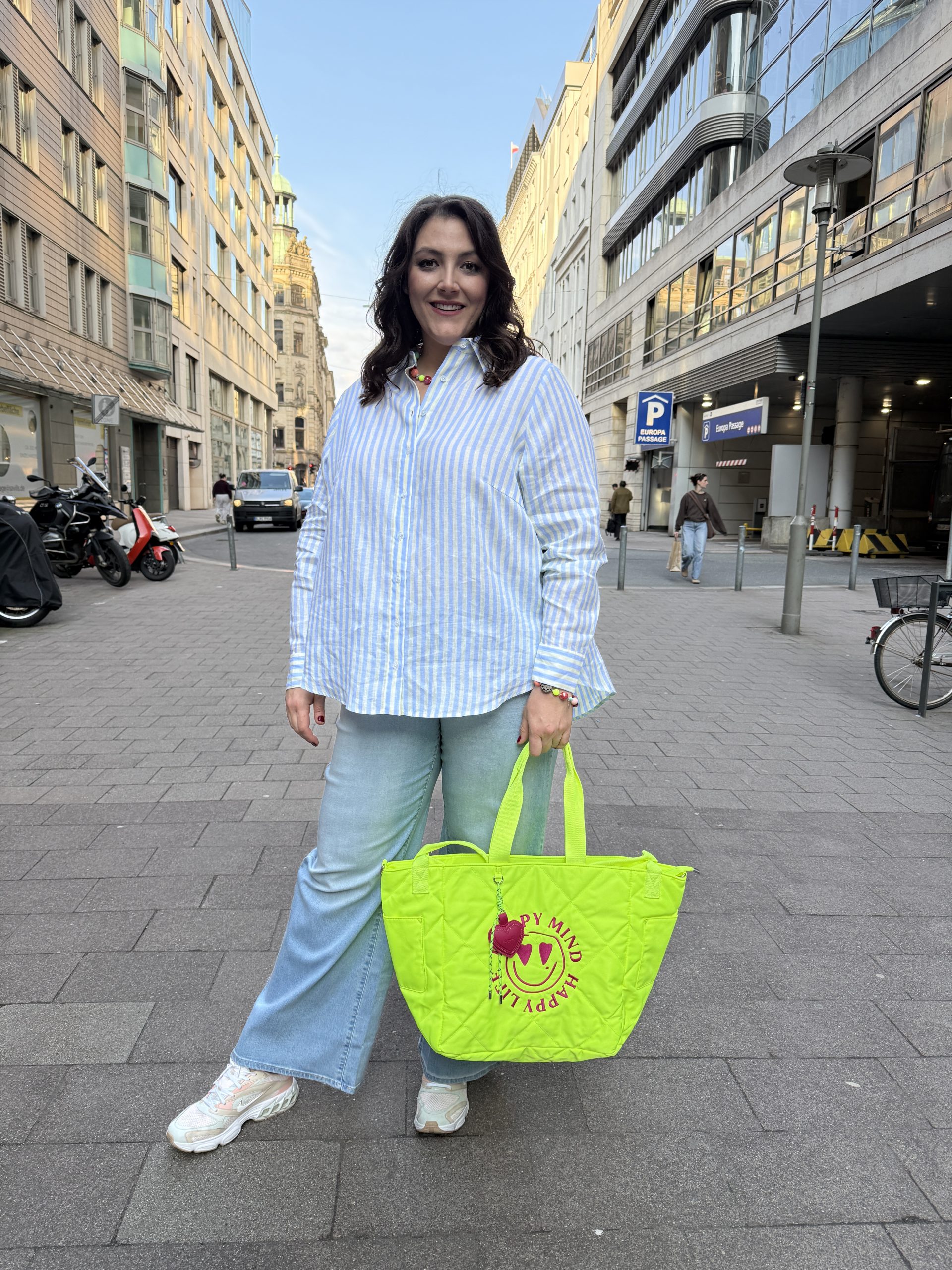 Mode für Mollige in Stuttgart: Frau trägt gestreifte Oversize-Bluse mit heller Jeans und neonfarbener Tote Bag