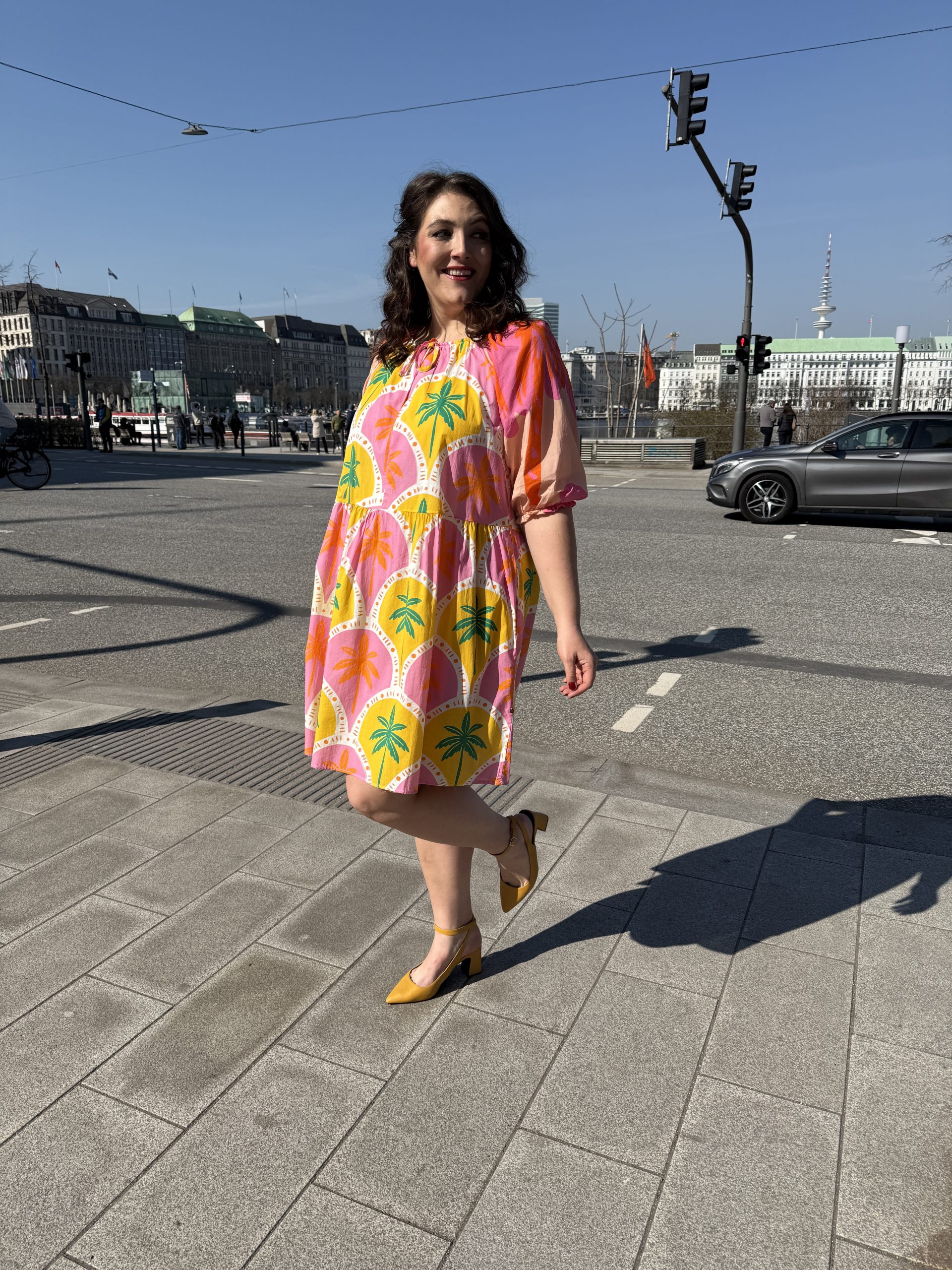 Übergrößen Lübeck: Frau trägt buntes Oversized-Kleid mit Palmenprint und gelben Slingback-Pumps im Streetstyle