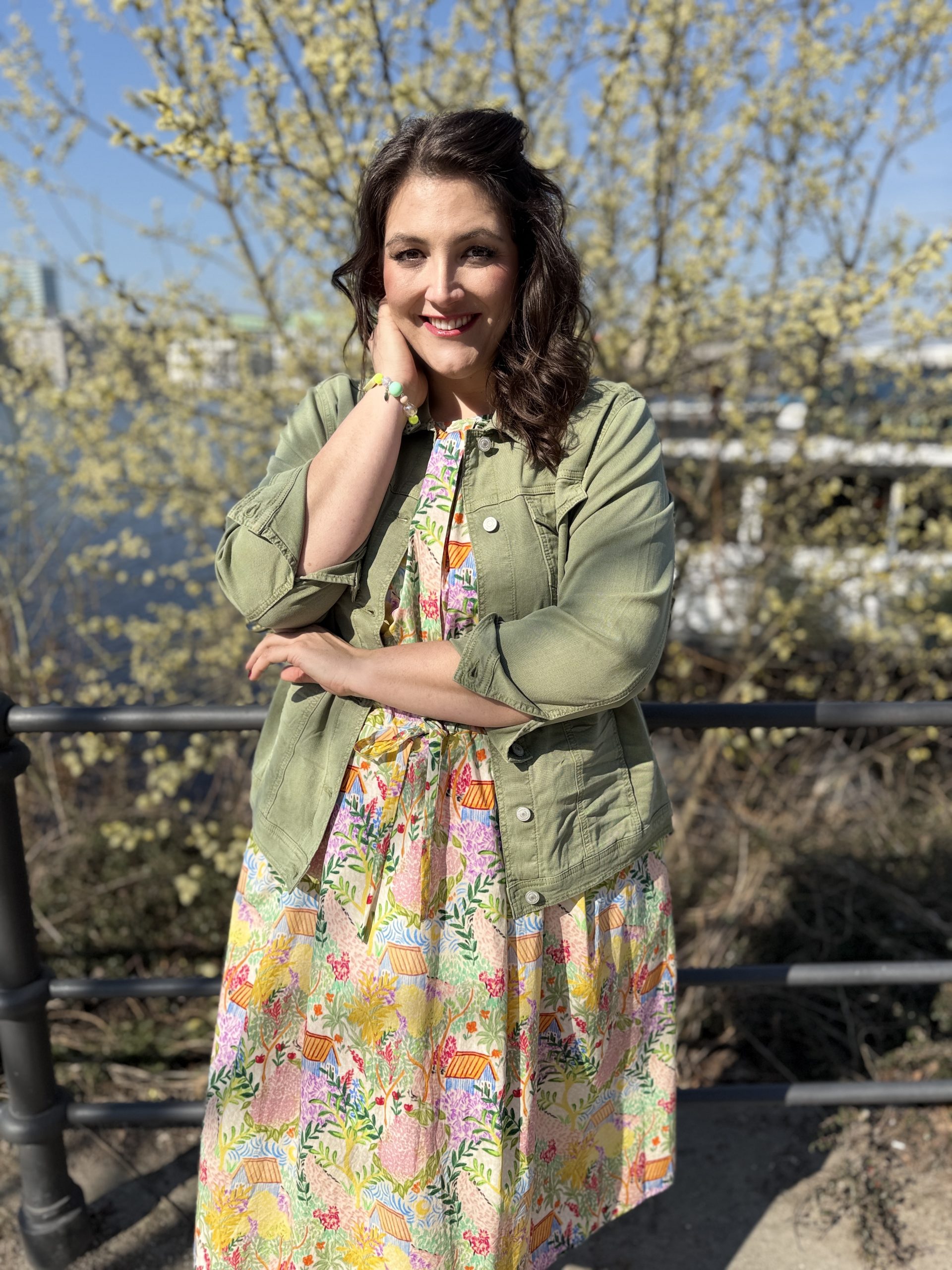 Mode für Mollige in Essen: Frau trägt buntes Sommerkleid mit olivgrüner Jeansjacke im Frühlings-Streetstyle
