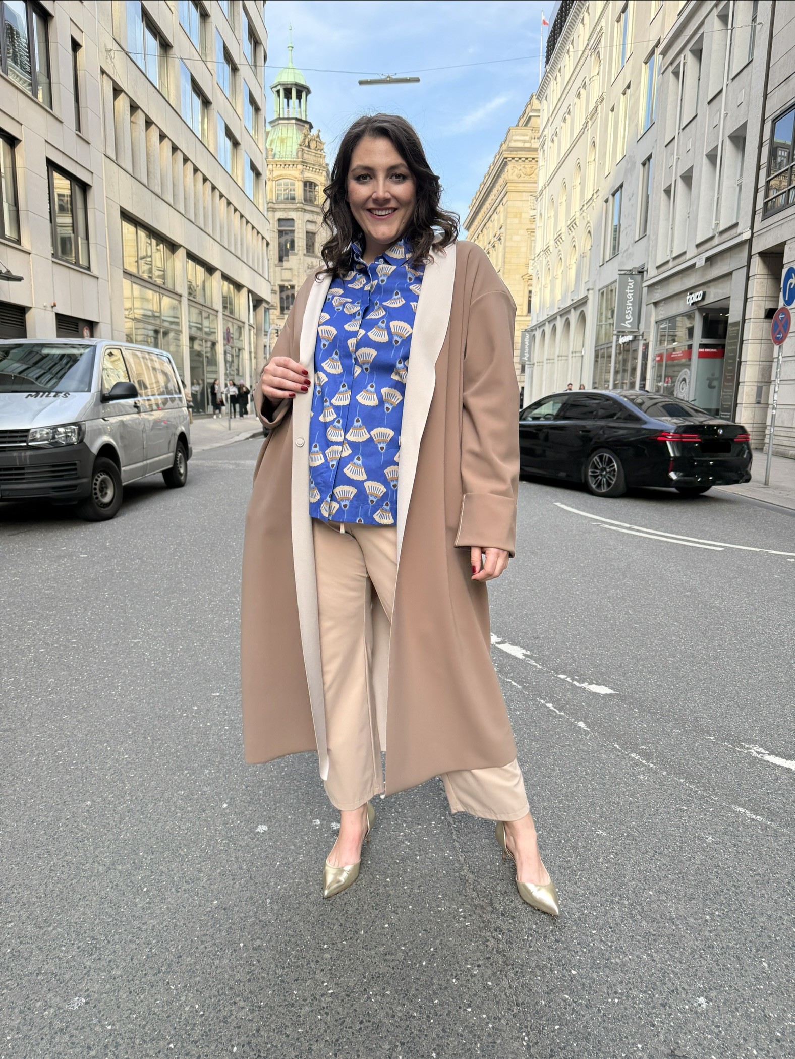 Mode für Mollige in Hamburg: Frau trägt beigen Longcoat, blaue Musterbluse und goldene Pumps