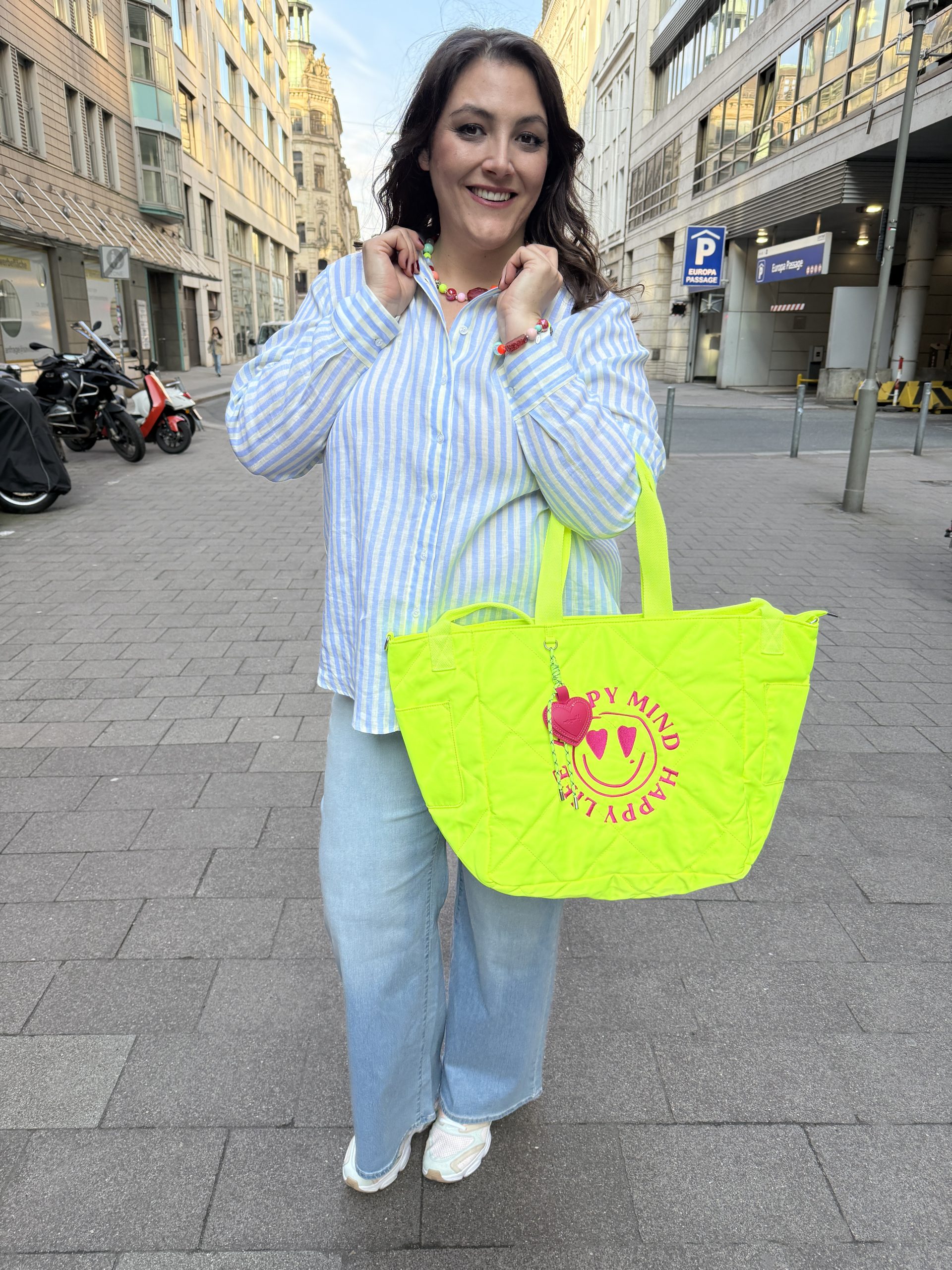 Mode für Mollige in Hannover: Frau trägt gestreifte Bluse, helle Jeans und neonfarbene Tote Bag